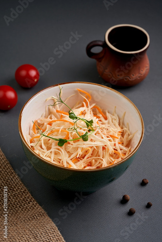 Obraz na płótnie Shredded cabbage and carrot salad garnished with pea sprouts in a ceramic bowl on a dark grey background