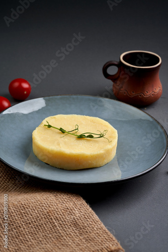 Round portion of mashed potatoes garnished with microgreens on a blue ceramic plate, dark grey background.