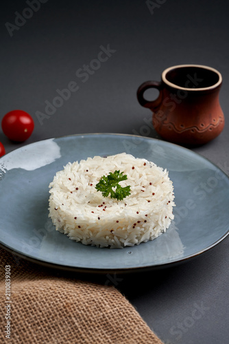 Round portion of cooked white rice decorated with parsley on a blue ceramic plate, dark grey background.