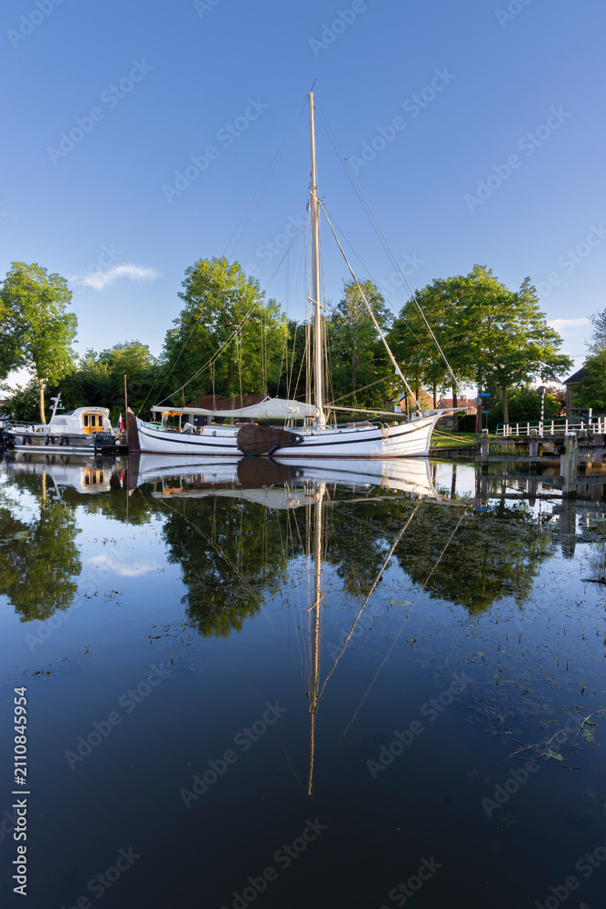 Fototapeta premium Sailboat moored on a calm canal with perfect reflection in Dokkum Friesland Netherlands town harbor