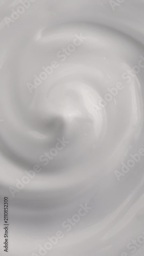 White Cream Swirling. Thick glossy cream moves in smooth folds, creating a soft abstract cosmetic texture.	