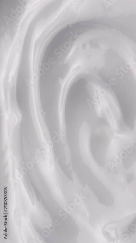 White Cream Swirling. Thick glossy cream moves in smooth folds, creating a soft abstract cosmetic texture.	