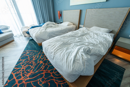 Bild auf Leinwand Twin beds and a rollaway extra bed with untidy bedding, a recently occupied family hotel room