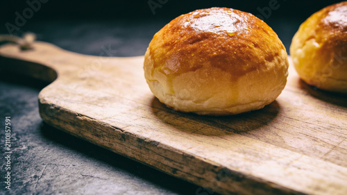 Fresh baked golden brown dinner rolls on rustic wooden cutting board