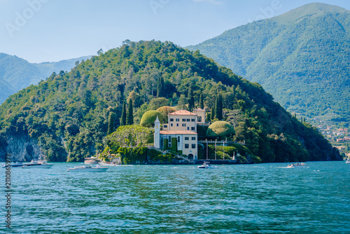 Scenic view of a villa on a lush green island surrounded by the tranquil waters of Lake Como, with mountains in the background