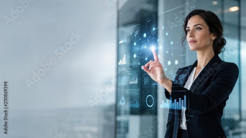 professional woman interacts with a transparent digital interface displaying futuristic data and graphs in a modern office setting.