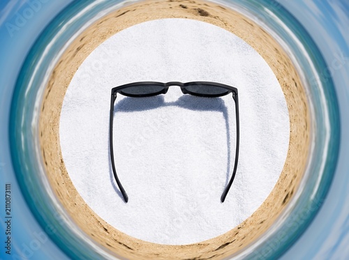 Stylish black sunglasses resting on a white sandy beach with ocean waves in the background.