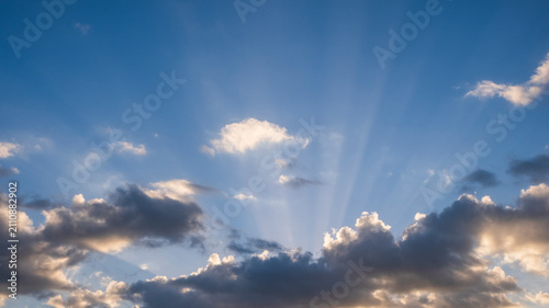 Photos Crepuscular sun rays spreading across a bright blue sky with fluffy white clouds