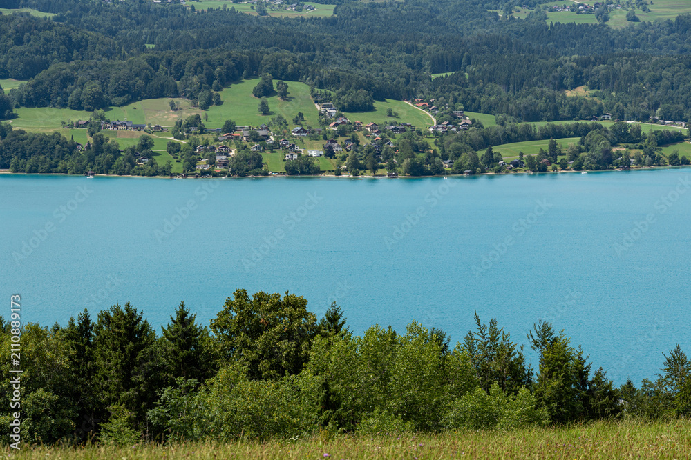 Fototapeta premium Turquoise alpine lake with lakeside village and forested hills