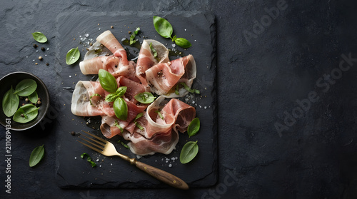 Overhead View of Thinly Sliced Prosciutto with Fresh Basil Leaves and Pine Nuts on Slate Board