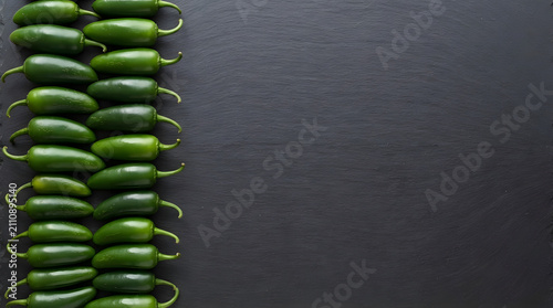 Fresh Green Jalapeño Peppers Lined Up on Slate Surface with Copy Space