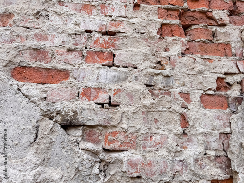 Obraz na plátne Damaged brick wall with crumbling red bricks and deteriorating white plaster sur