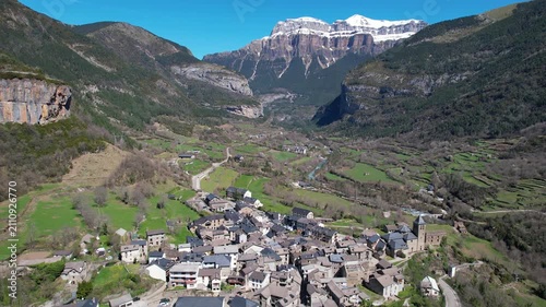 Drone footage of Torla-Ordesa village and covered with snow mountains of Ordesa y Monte Perdido National Park on sunny spring day. Huesca, Spain.