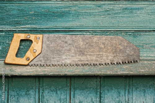 Картината върху платно one old iron gray hacksaw with a yellow wooden handle lies on a green table