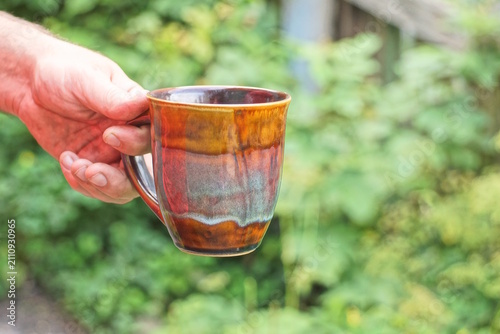 hand holding one big brown ceramic cup on green background in the street
