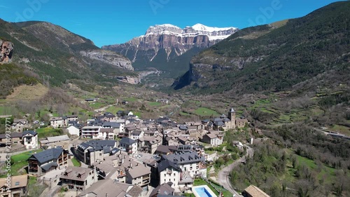 Forward reveal aerial footage of Torla-Ordesa village and covered with snow mountains of Ordesa y Monte Perdido National Park on sunny spring day. Huesca, Spain.