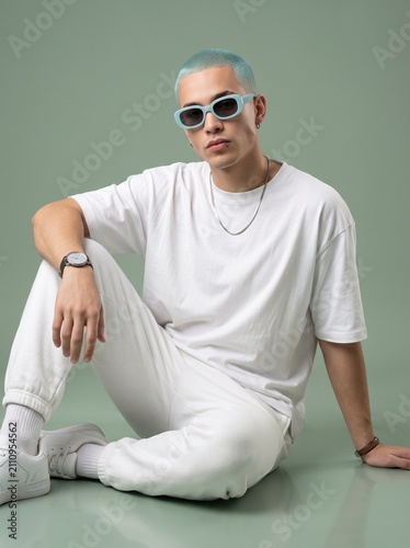 Stylish young adult male sitting on studio floor in blank white t-shirt for mockup