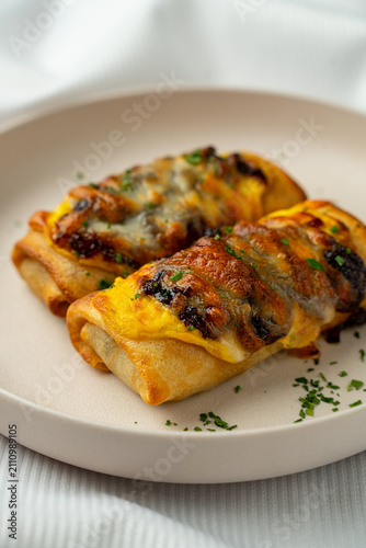 A plate holds two enchiladas filled with cheese and covered in a light sauce. The dish shows hints of green herbs scattered around it. The setting suggests a casual dining place