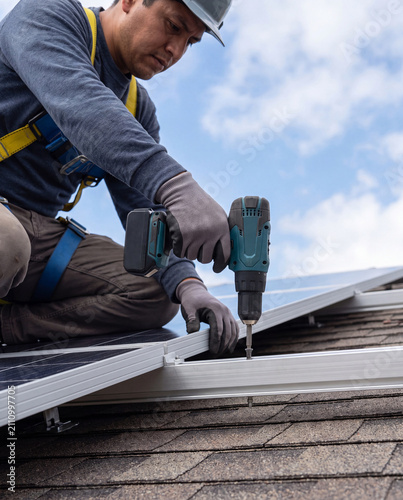 Solar panel installer using cordless drill to fasten mounting rail on shingled roof