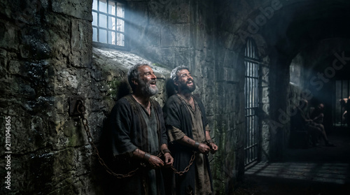 Apostles Paul and Silas praying and singing hymns in a dark, grimy prison cell just before a miraculous earthquake strikes