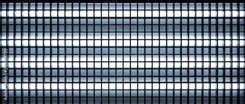 Grid of fluorescent lights in a ceiling panel creating a bright illuminated abstract pattern with dark grid.