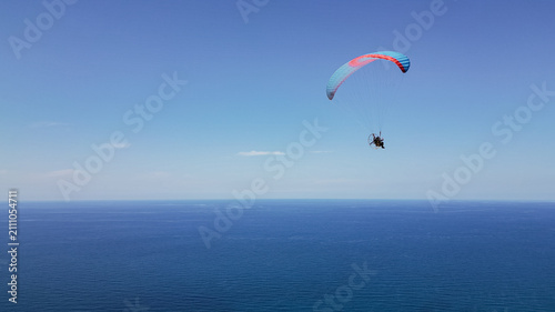 Canvastavla Side view photo of powered paraglider in red and blue canopy flying over deep se