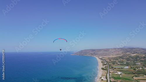 Принти на полотні Aerial view of powered paraglider flying over blue sea water along coastal line
