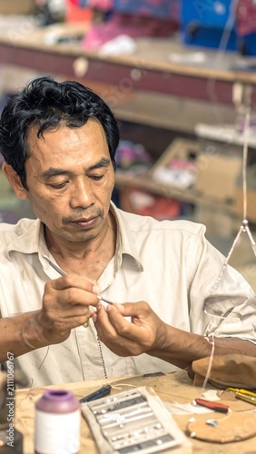 An artisan, focused, meticulously crafts a delicate object at a workbench, with tools and materials. His face reflects concentration