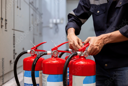 Professional technician checking and inspecting pressure gauge of red fire extinguishers for annual safety maintenance and compliance in industrial building.