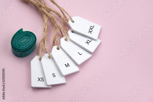 Various clothing sizes XS, S, M, L, XL on white wooden tags on the pink background.