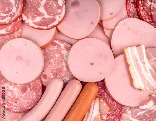 Full background texture of scattered processed deli meats and shiny round bologna slices.