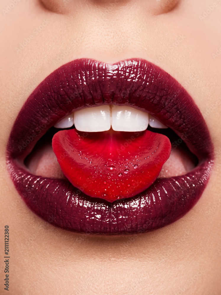 Fototapeta premium Glossy berry lips holding a red rose petal, representing passionate New Year romance and luxury holiday beauty campaigns.