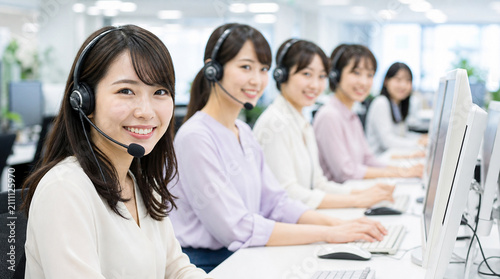 笑顔で対応するヘッドセット姿の日本人女性コールセンターチーム
Group of smiling Japanese female call center operators wearing headsets in a bright modern office