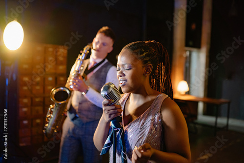 Obraz na płótnie Soulful Black woman sings vintage jazz at an intimate bar performance, accompani