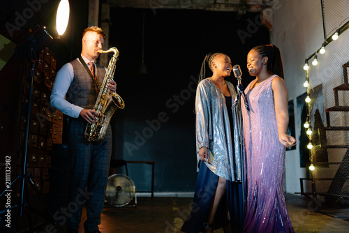 Photography A male saxophonist and two female singers perform live jazz in a stylish, warm-l