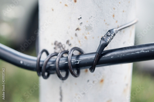 Obraz na płótnie Bicycle secured with a coiled cable combination lock wrapped around its frame and a metal pole in an urban setting