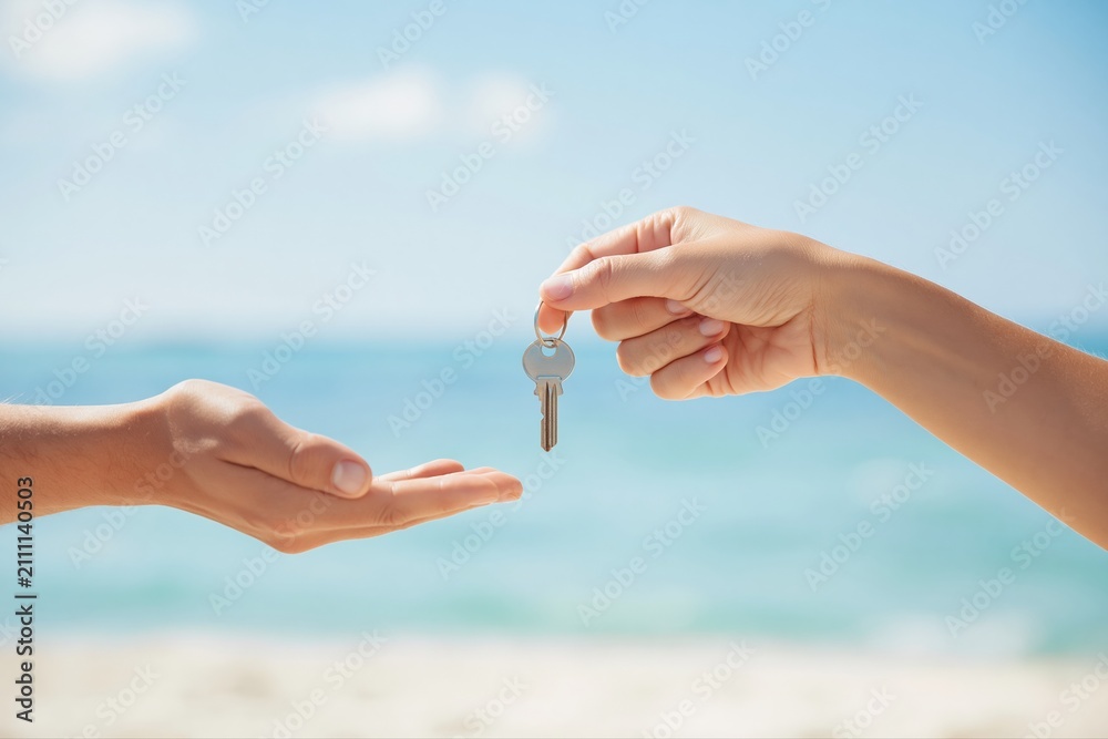 Obraz premium Handing over a single house key on a sunny beach, symbolizing vacation home ownership and transfer