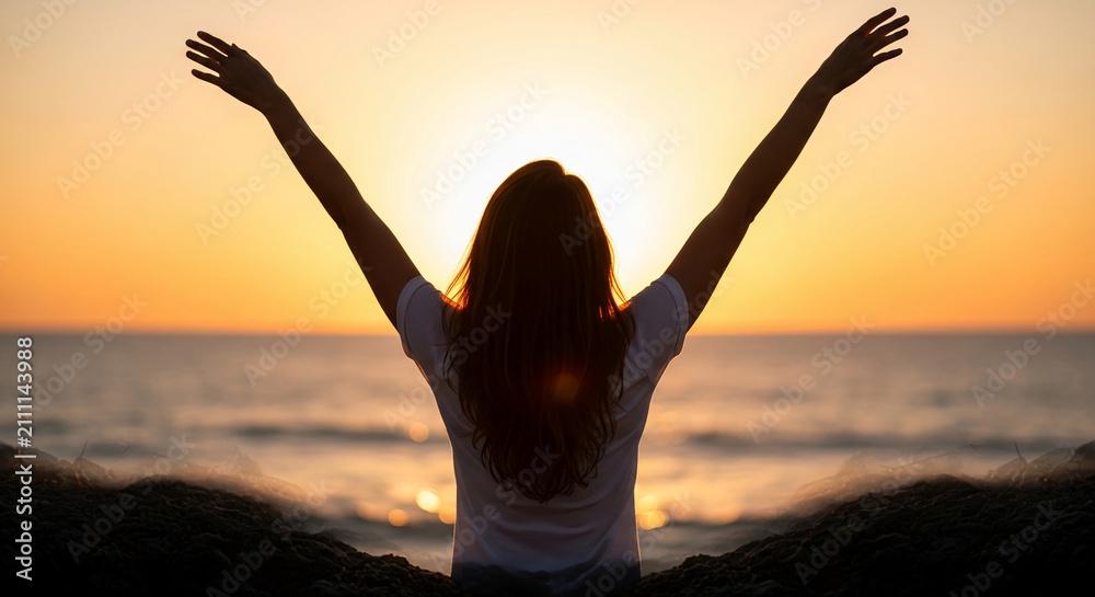 Fototapeta premium Silhouette of person with arms raised against a golden sunset over the ocean, symbolizing freedom, joy, and hope.