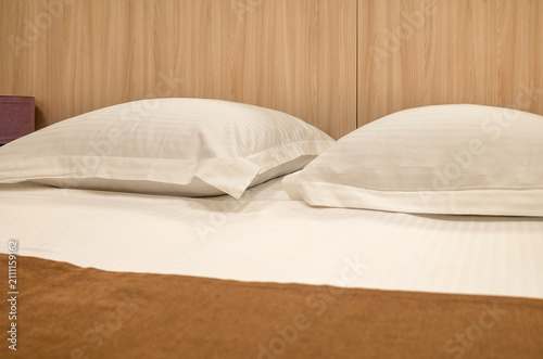 Quadro su tela Two white pillows on bed against wooden headboard background