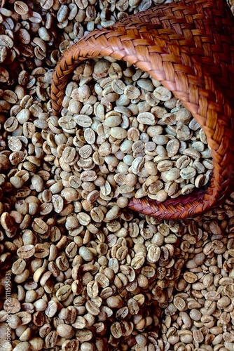  Raw unroasted green coffee beans being poured into a traditional wooden hopper during the specialty coffee processing and roasting workflow.