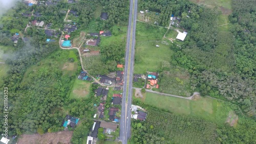 Aerial view of drone flying over countryside village with road through green forest and light morning fog.Cinematic shot of rural village nestled in mountains with a road winding through mist.