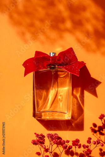 Fragrance bottle with red bow placed on orange background surrounded by small flowers
