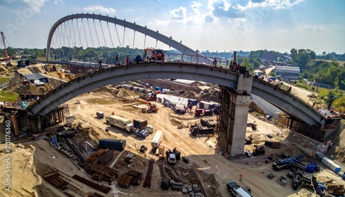 Modern Bridge Construction: Arch Structure and Cable-Stayed Elements Underway with Heavy Machinery and Workers