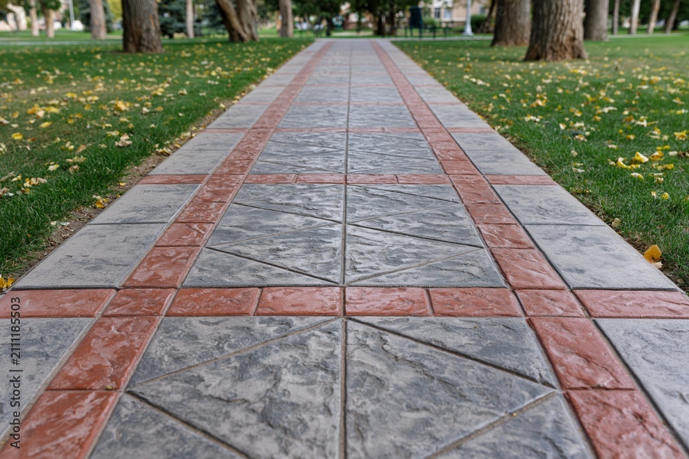 Obraz premium The Stone Tiled Path Through a Park with Red Brick Borders