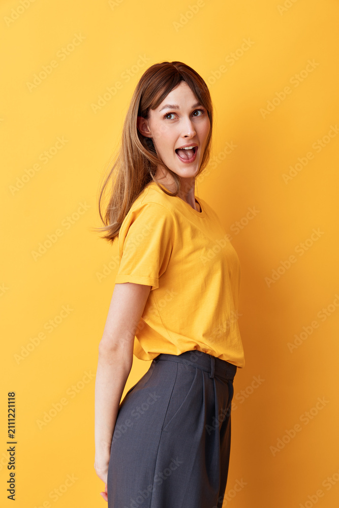 Obraz premium Smiling woman with brown hair wearing a yellow shirt, standing against a yellow background. Bright, cheerful mood, fashion portrait, casual style, studio lighting.
