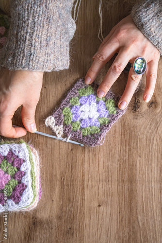 Close up of hands joining granny squares into one fabric. Crochet project in progress. Craft process, handmade fashion creation and slow creative lifestyle concept.