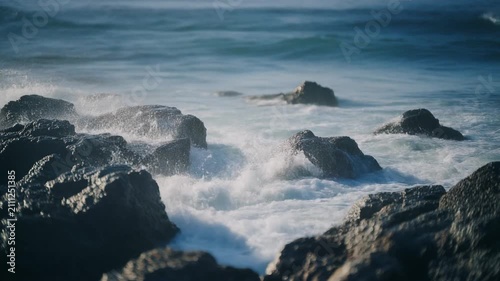 Dynamic ocean waves relentlessly crash against the weathered rocks of a rugged coastline, creating a mesmerizing spectacle of water and stone