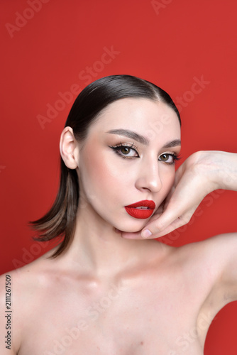 A beautiful woman with bright red lips and dark hair against a bright red background.