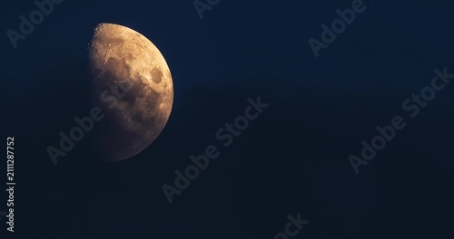First quarter moon rising through dark blue twilight clouds time lapse