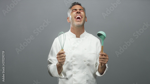 Foto Man chef holding whisk and ladle, mouth open and head tilted back in a studio; playful exuberance joy